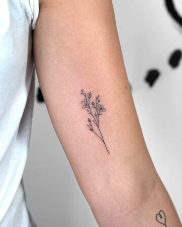 Delicate fine line floral tattoo on a woman's arm, featuring small, minimalist flowers and buds. The tattoo is a simple, elegant design, a perfect example of a small floral tattoo. Done by tattoo artists in our fine line tattoo studio parlour shop Canggu, Bali