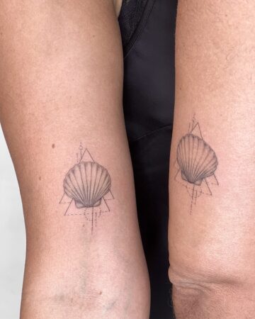 Two arms side-by-side, each displaying a matching minimalist sea shell tattoo. The delicate line art depicts a scallop shell within a geometric triangle and lines, perfect for couples tattoos. The design is a beautiful example of matching tattoos. Done by tattoo artists in our fine line tattoo studio parlour shop Canggu, Bali