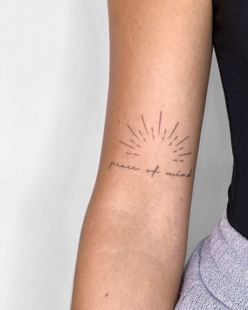 Delicate sunburst tattoo on an arm, with the words "peace of mind" in elegant script. A visual reminder of the importance of mindfulness and self-care. Done by tattoo artists in our fine line tattoo studio parlour shop Canggu, Bali