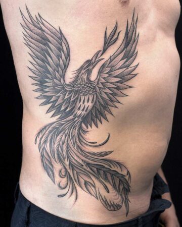 A detailed black and grey phoenix tattoo on a person's side, wings outstretched in flight. The bird tattoo features intricate feather detailing and a dynamic pose, showcasing tattoo ideas for a striking side tattoo. Done by tattoo artists in our fine line tattoo studio parlour shop Canggu, Bali