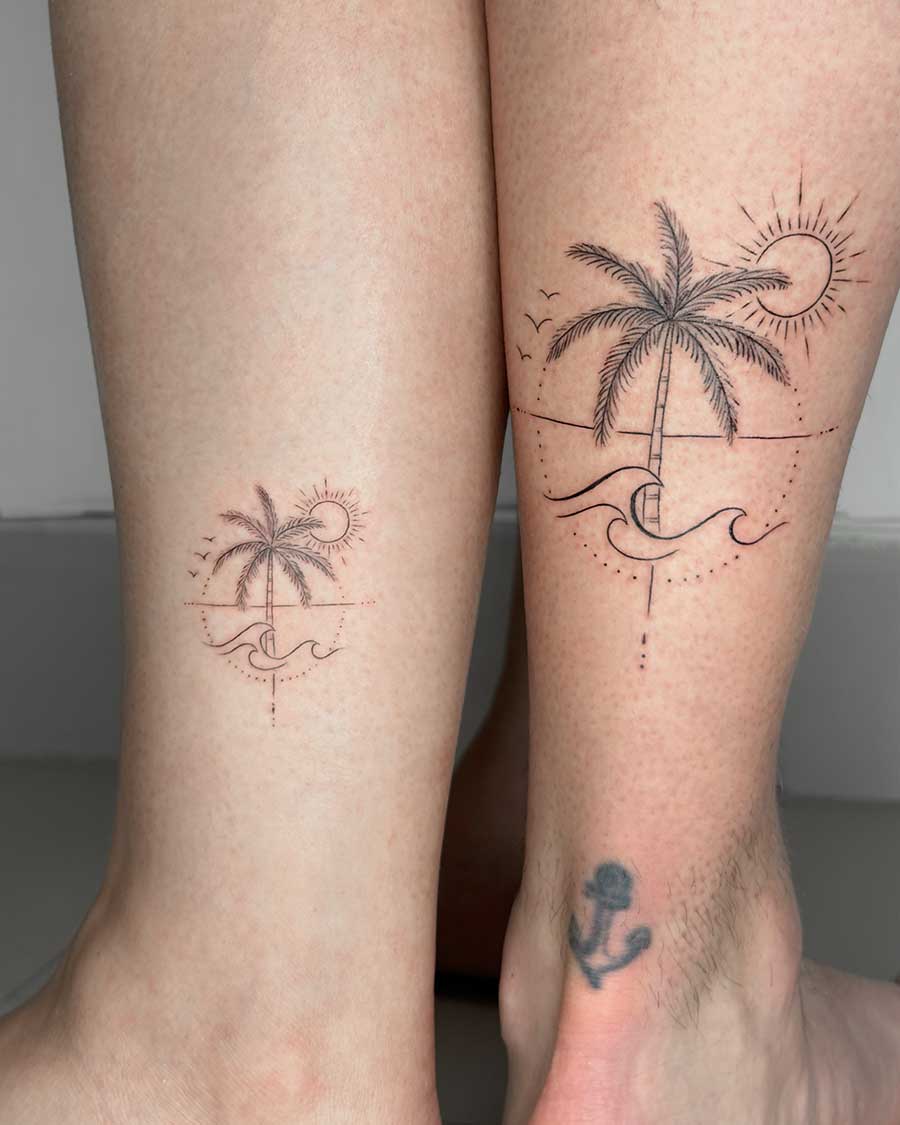 Matching tattoos on legs: a palm tree scene with sun and waves, one larger than the other. Couples tattoo inspiration. Created by expert tattoo artists in Canggu Bali.