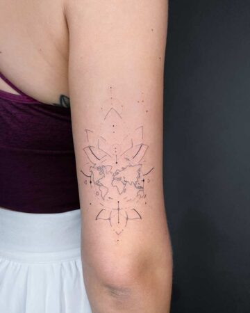 Delicate world map tattoo in a geometric floral design on an arm. This minimalist tattoo features fine lines and dots, set against a dark background, showcasing tattoo art and design. Done by tattoo artists in our fine line tattoo studio parlour shop Canggu, Bali
