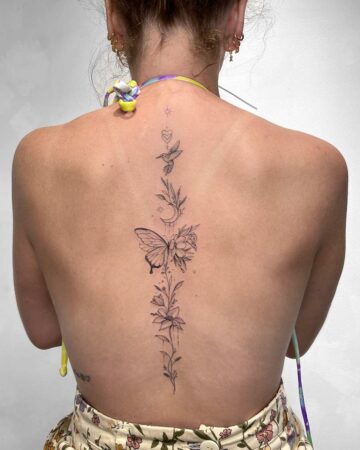 Woman's back featuring a delicate spine tattoo. The design includes a butterfly, flowers, a hummingbird, and a crescent moon, showcasing a minimalist and floral tattoo style. This back tattoo is perfect for tattoo inspiration. Done by tattoo artists in our fine line tattoo studio parlour shop Canggu, Bali