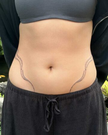Close-up of a person's midsection featuring delicate, flowing black ink tribal tattoos on the hips, resembling abstract waves or vines, set against smooth skin. Created in the multi style tattoo studio in Canggu Bali, Bali tattoo, Canggu tattoo studio.