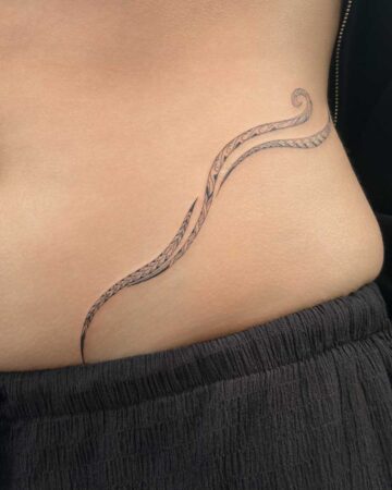 Close-up of a delicate black tribal-inspired tattoo on a person's lower back, featuring flowing lines and intricate patterns, created in the multi style tattoo studio in Canggu Bali. Bali tattoo artists provide unique designs.
