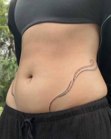 Close-up of a woman's midsection featuring a delicate, flowing tribal-inspired tattoo design wrapping around her waist. Created in the multi style tattoo studio in Canggu Bali, Bali tattoo studio, best tattoo Canggu.