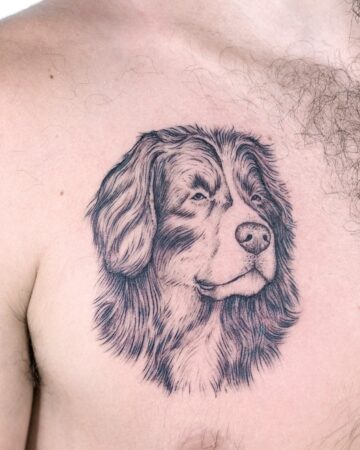 A detailed black and white dog tattoo on a person's chest, featuring a realistic portrait of a Bernese Mountain Dog. The dog's fur is meticulously shaded, showcasing a pet portrait tattoo design. Done by tattoo artists in our fine line tattoo studio parlour shop Canggu, Bali