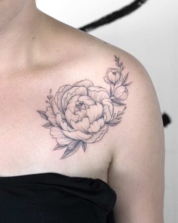 Delicate peony tattoo on a woman's shoulder. The black and white floral design features a large, detailed peony blossom with smaller buds and leaves, showcasing a fine line tattoo style. A beautiful example of a peony tattoo. Done by tattoo artists in our fine line tattoo studio parlour shop Canggu, Bali