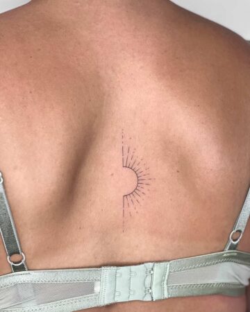 Minimalist sun tattoo design on a woman's back. The tiny tattoo features a half-sunburst pattern and is a great example of a minimalist tattoo. This back tattoo is a perfect example for tiny tattoo ideas. Done by tattoo artists in our fine line tattoo studio parlour shop Canggu, Bali