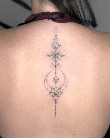 Delicate minimalist tattoo on a woman's back, featuring a compass design and lotus flowers. The tattoo is a vertical composition with fine lines, showcasing intricate details and a modern aesthetic. Done by tattoo artists in our fine line tattoo studio parlour shop Canggu, Bali