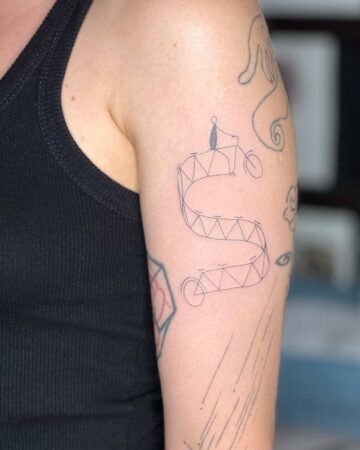 Minimalist line art tattoo on arm depicting a person riding a bicycle on a zig-zag path, a unique example of tattoo art. Other small tattoos are also visible. Done by tattoo artists in our fine line tattoo studio parlour shop Canggu, Bali