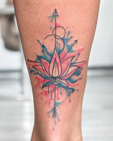 A vibrant watercolor lotus flower tattoo on a leg. The design features a pink and blue lotus with geometric lines, arrows, and splattered watercolor effects, showcasing a modern floral tattoo style.