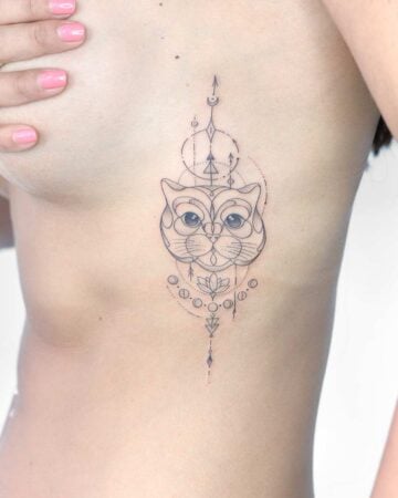 Delicate geometric cat tattoo on a woman's side. The minimalist design features a cat's face, circles, arrows, and a lotus flower, showcasing a unique geometric tattoo style. Done by tattoo artists in our fine line tattoo studio parlour shop Canggu, Bali