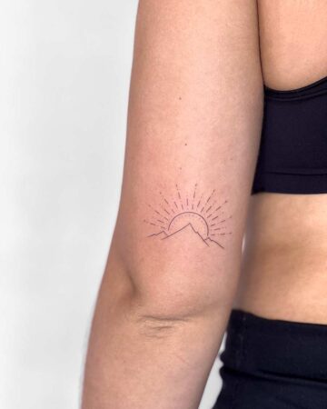 Delicate minimalist mountain tattoo featuring a rising sun, inked on the inner arm. A subtle sun tattoo design, perfect for mountain tattoo enthusiasts. Done by tattoo artists in our fine line tattoo studio parlour shop Canggu, Bali