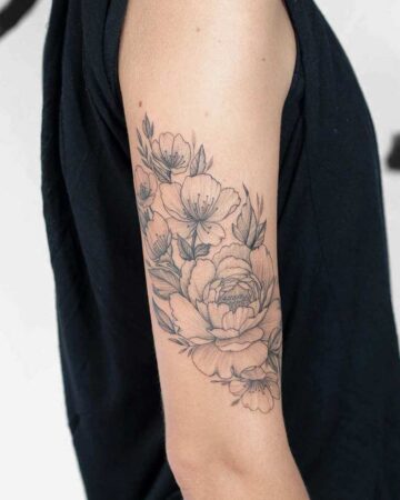 Floral tattoo design on a woman's arm featuring detailed peony and other delicate blossoms with leaves. The black ink artwork elegantly curves around the arm.