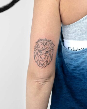 Geometric lion tattoo design on an arm. The minimalist tattoo features a detailed lion head, inked in black, on the inner arm. Ideal lion tattoo idea. Done by tattoo artists in our fine line tattoo studio parlour shop Canggu, Bali