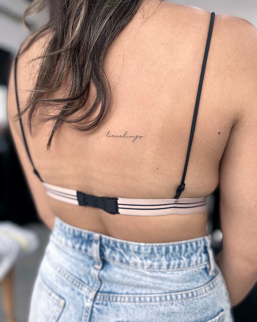 Woman's back with delicate "leveling up" script tattoo. Minimalist tattoo design.