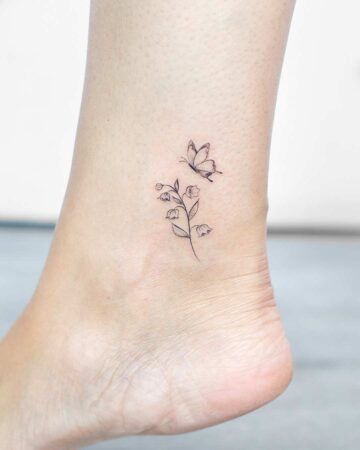 Delicate ankle tattoo featuring a sprig of Lily of the Valley with a tiny butterfly perched above. Fine line art gives a minimalist, elegant look.