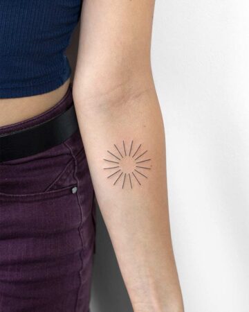 Minimalist sun tattoo on a forearm, featuring thin black lines radiating from a central point. A simple, small tattoo design. Done by tattoo artists in our fine line tattoo studio parlour shop Canggu, Bali