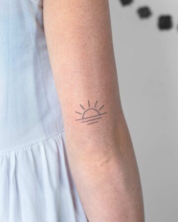 Minimalist tattoo of a sunrise on a woman's arm. The simple line art shows the sun rising over water, inked in black on fair skin.