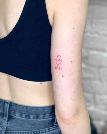 Red tattoo on arm says "No More Sad Days" promoting a positive mindset.