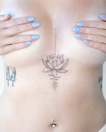 Woman's torso featuring a delicate lotus flower tattoo between her breasts, extending upwards with a line and dots, and downwards with a spiral design. Additional small tattoos are visible on her sides. Blue nail polish.