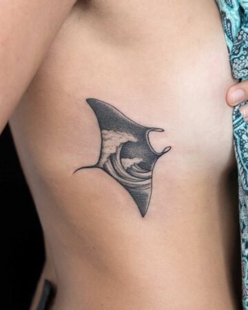 Black and grey tattoo of a manta ray with a wave design inside its body, inked on a person's side. A unique black and grey tattoo design.