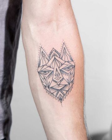 Geometric tattoo bali barong mask on forearm featuring a minimalist, abstract face composed of lines, triangles, and dotwork. This geometric tattoo is a striking example of tattoo ideas. Done by tattoo artists in our fine line tattoo studio parlour shop Canggu, Bali