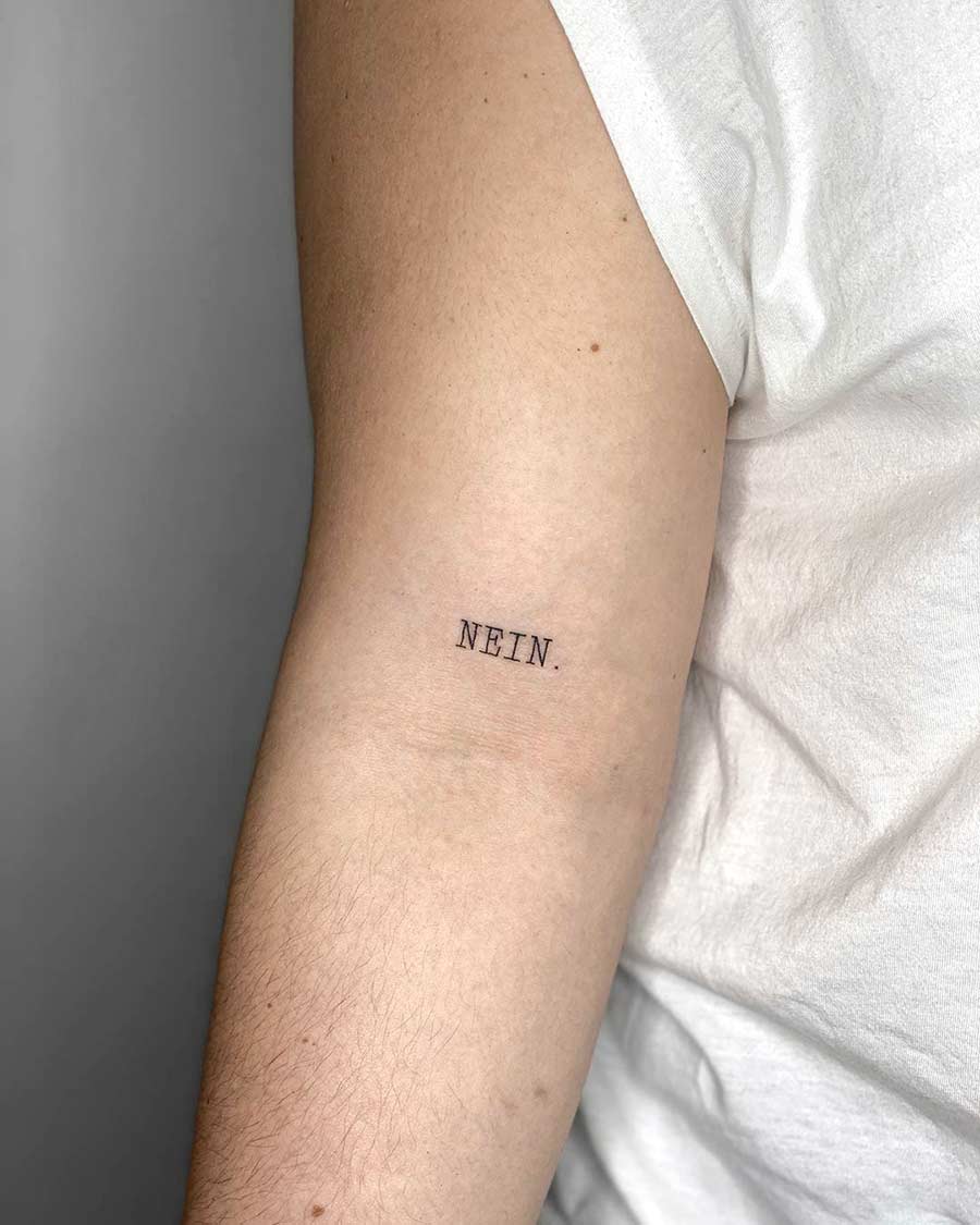 Close-up of an arm with a small, minimalist tattoo that reads "NEIN." in a simple, sans-serif font.