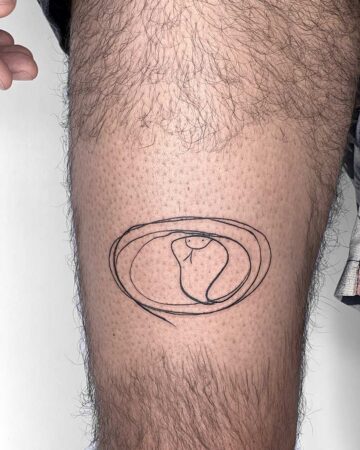 A minimalist snake tattoo on a hairy leg. The simple line art depicts a coiled snake with a smiling face, encircled by a scribbled outline, a quirky design for a leg tattoo. Done by tattoo artists in our fine line tattoo studio parlour shop Canggu, Bali