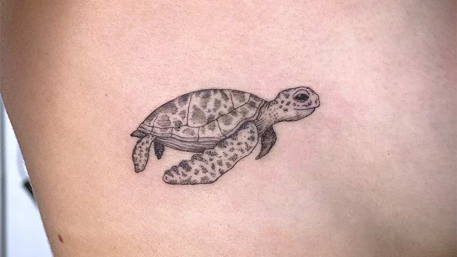 Delicate turtle tattoo on a person's side. The small tattoo features intricate dotwork shading on the shell and flippers, a minimalist design. Perfect inspiration for small tattoos and minimalist tattoos. Done by tattoo artists in our fine line tattoo studio parlour shop Canggu, Bali