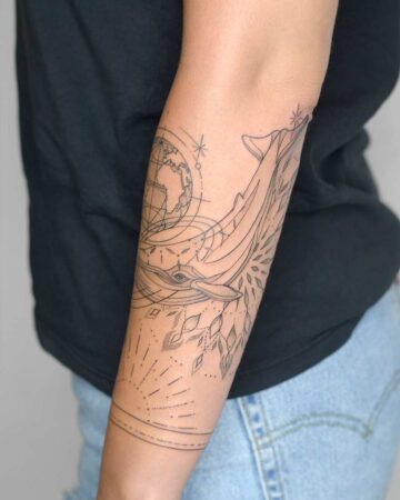 Detailed minimalist whale tattoo on an arm, featuring a globe, stars, and sunburst design. This nature-inspired whale tattoo showcases a beautiful blend of geometric and organic elements, perfect for those seeking a unique arm tattoo. done by artists in our fine line tattoo studio Canguu Bali
