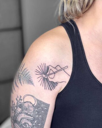 Minimalist line art tattoo on a shoulder, depicting a hand holding a tool with radiating lines, possibly representing welding or creating. The tattoo is a small, black, and simple design, showcasing a creative arm tattoo. Done by tattoo artists in our fine line tattoo studio parlour shop Canggu, Bali