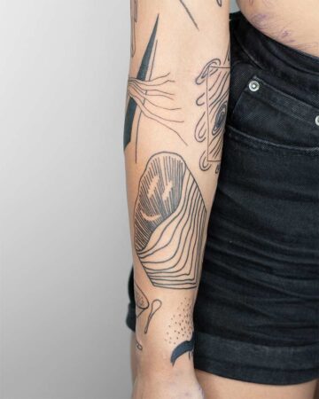 Close-up of an arm covered in various minimalist black ink tattoos. The designs include a geometric shape, abstract lines, and a mountain-like form, showcasing a modern tattoo style. Done by tattoo artists in our fine line tattoo studio parlour shop Canggu, Bali