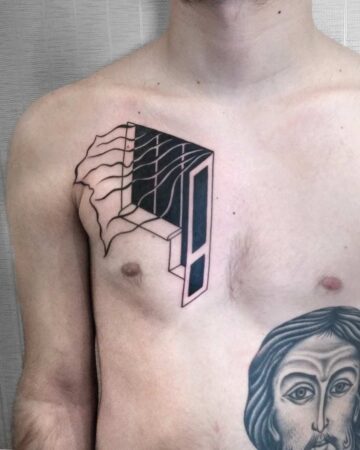 A man's chest featuring a striking geometric tattoo. The black ink design depicts a stylized window or portal with flowing lines, creating a unique and artistic chest tattoo. Below, a religious figure tattoo is also visible. done by artists in our fine line tattoo studio Canguu Bali