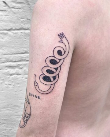 Minimalist tattoo of a coiled snake with a hand at the top, inked on an arm. The snake has a smiling face, with the word "TRUNK" inked below a different tattoo. The body art is a simple black line design. done by artists in our fine line tattoo studio Canguu Bali