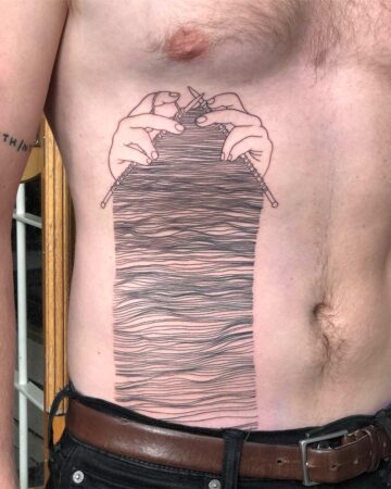 A torso with a striking tattoo of hands knitting, the needles holding a rectangular section of wavy horizontal lines. The design covers the upper abdomen and chest, a creative display of body art and unique tattoo ideas. Done by tattoo artists in our fine line tattoo studio parlour shop Canggu, Bali