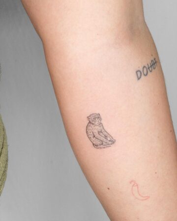 A detailed, minimalist monkey tattoo sits on the arm, alongside "DOUBT" text and a red chili pepper tattoo. Perfect for tiny tattoo inspiration. Done by tattoo artists in our fine line tattoo studio parlour shop Canggu, Bali