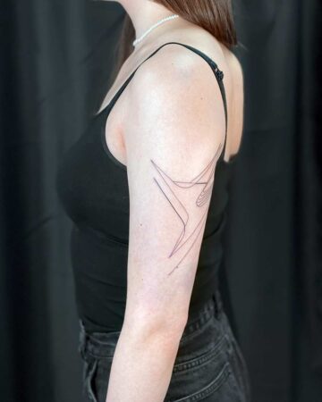 A woman's arm featuring a minimalist line art tattoo. The black ink design is a geometric star-like shape, a great example of a small, minimalist tattoo. She wears a black tank top and jeans.