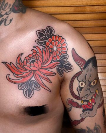 Chest and shoulder tattoo featuring traditional Japanese chrysanthemum flowers in vibrant red with black leaves, alongside a grey oni mask tattoo. Japanese (Irezumi/Wabori) tattoo artist studio Canggu Bali