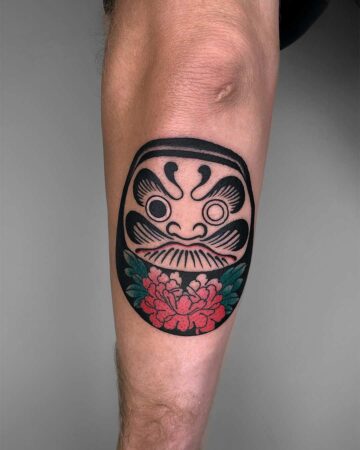 Close-up of a traditional Japanese Daruma doll tattoo on an arm, featuring bold black lines, a red peony flower, and intricate detailing. Japanese (Irezumi/Wabori) tattoo studio Canggu Bali