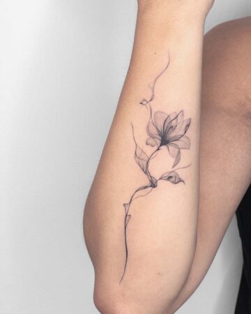 Delicate fine line floral tattoo on an arm. A minimalist design features a stylized flower and leaves, with wispy lines creating a soft, ethereal effect. This elegant arm tattoo showcases the beauty of a fine line tattoo.