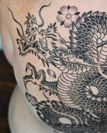 Detailed black and grey Japanese dragon tattoo with cherry blossoms on a person's skin. The dragon's scales and fierce expression are prominently displayed.