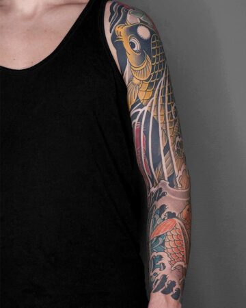 Elaborate Japanese koi fish tattoo sleeve on a person's arm, featuring vibrant gold and orange scales, wave patterns, and traditional artistic style. Japanese (Irezumi/Wabori) tattoo artist studio Canggu Bali