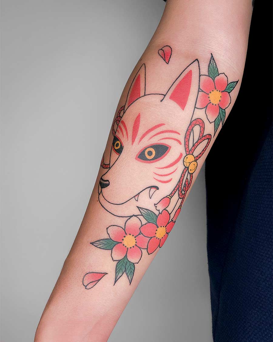 Forearm tattoo of a Kitsune mask with red accents, cherry blossoms, and a decorative rope. The vibrant colors and traditional Japanese design make it a striking piece of body art. Japanese (Irezumi/Wabori) tattoo studio Canggu Bali