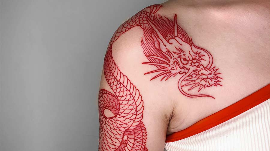 Red ink dragon tattoo winding from shoulder to upper arm. Intricate line work defines the scales and features of the mythical creature.
