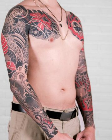 Torso shot of a man with a traditional Japanese dragon tattoo sleeve in gray and red, extending across his arms and chest. He wears khaki pants and a necklace. Japanese (Irezumi/Wabori) tattoo studio Canggu Bali