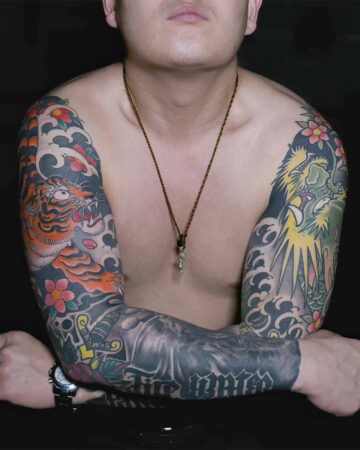 Torso shot of a man with full sleeve tattoos: a fierce tiger on one arm and a vibrant dragon on the other, accented with flowers and waves. Japanese (Irezumi/Wabori) tattoo artist studio Canggu Bali
