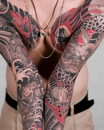 Torso with intricate Japanese dragon tattoos in red and black ink covering arms and chest. The detailed body art features waves and floral elements, enhanced by silver necklaces. Japanese (Irezumi/Wabori) tattoo artist studio Canggu Bali