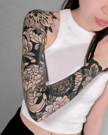 Woman with a striking black and white floral sleeve tattoo covering her entire arm, featuring chrysanthemums oriental japanese black and grey ink and mandala patterns